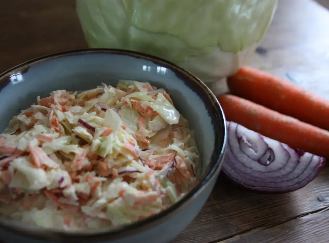 En skål med krämig coleslaw, gjord på kål, morötter och rödlök. Perfekt tillbehör för den godaste coleslaw.