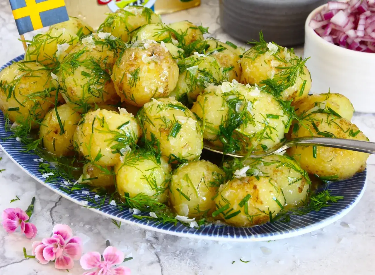 Nykokta, glansiga småpotatisar med dill och salt, redo att avnjutas. En svensk flagga vajar i bakgrunden.