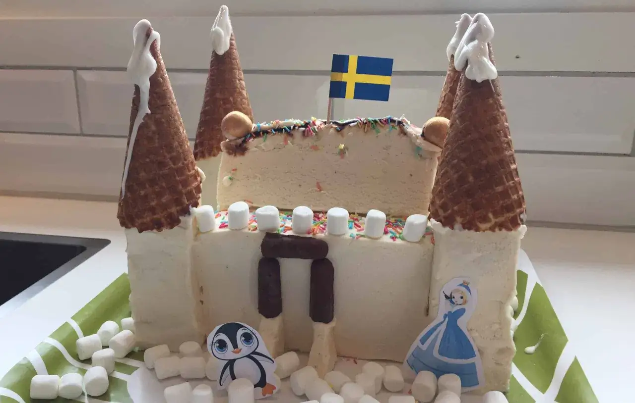 En fantasifull glasstårta formad som ett slott, perfekt för barn. Med svenska flaggan, pingvin och prinsessa.