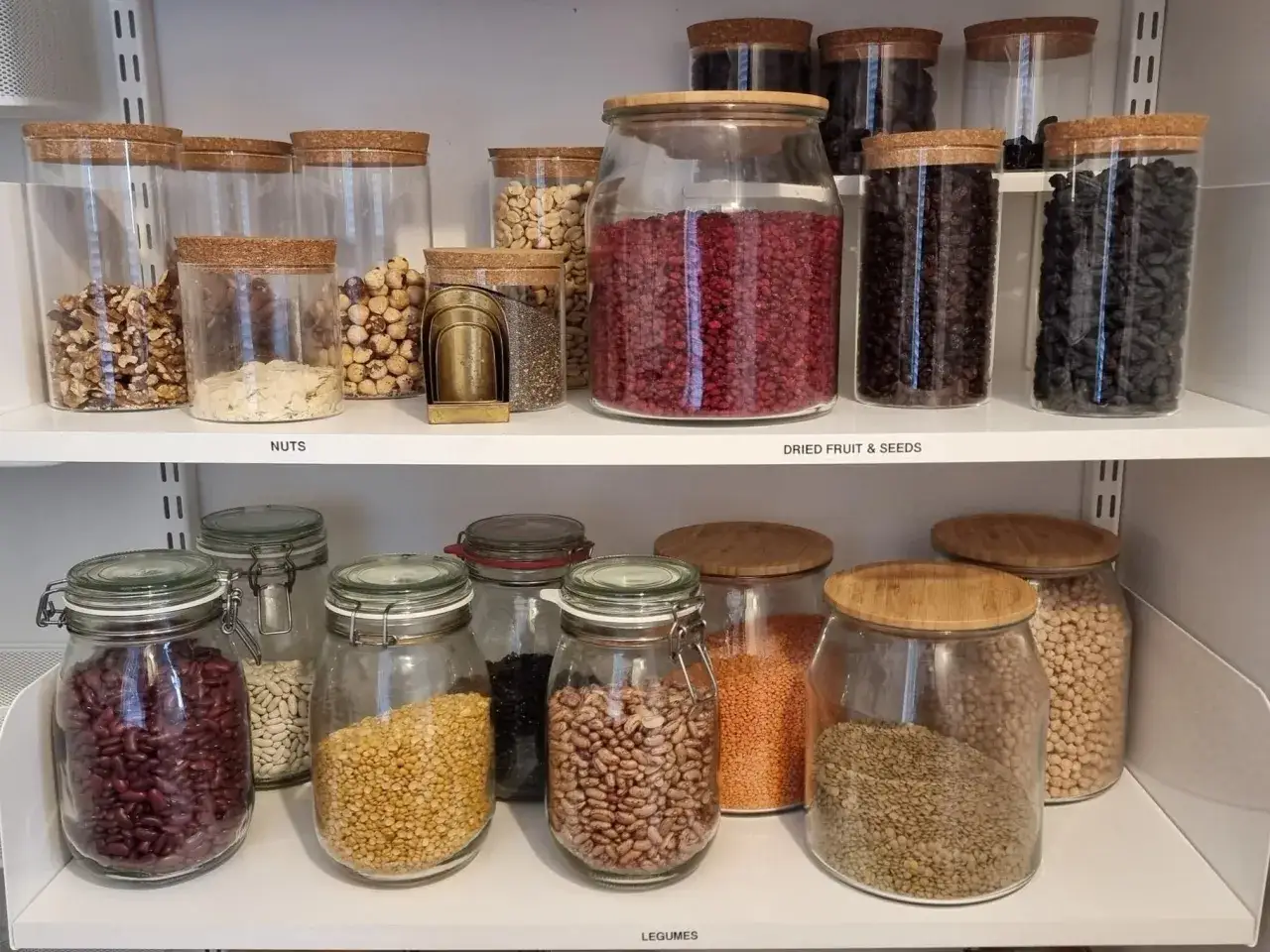 Hyllor fyllda med glasburkar med nötter, torkad frukt, frön och baljväxter. Perfekt för att ha basvaror att ha hemma.