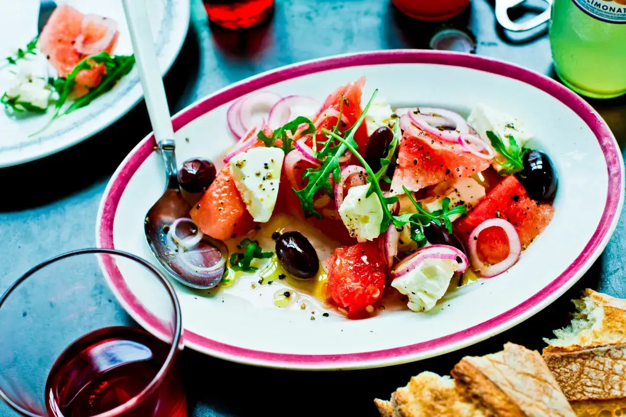 En uppfriskande melon och fetaostsallad med oliver och rödlök, serverad på en tallrik med en lila kant.