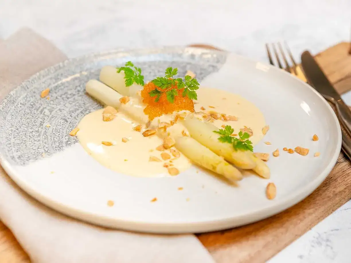 Vit sparris serveras med en krämig sås, orange rom och hackade nötter. En delikat rätt som hyllar vårens smaker.