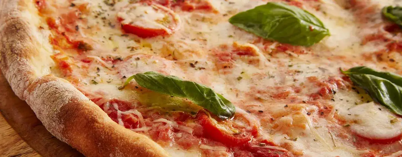 En närbild av en utsökt pizza med smält ost, tomater och färsk basilika. Perfekt för pizza dagen!