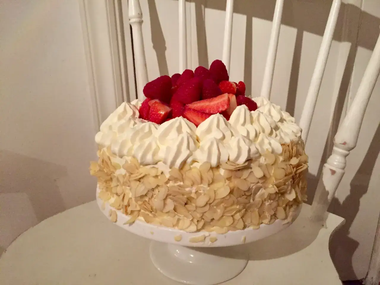En vacker tårta med vispgrädde, jordgubbar och hallon. Den har en glutenfri tårtbotten täckt med mandelspån.