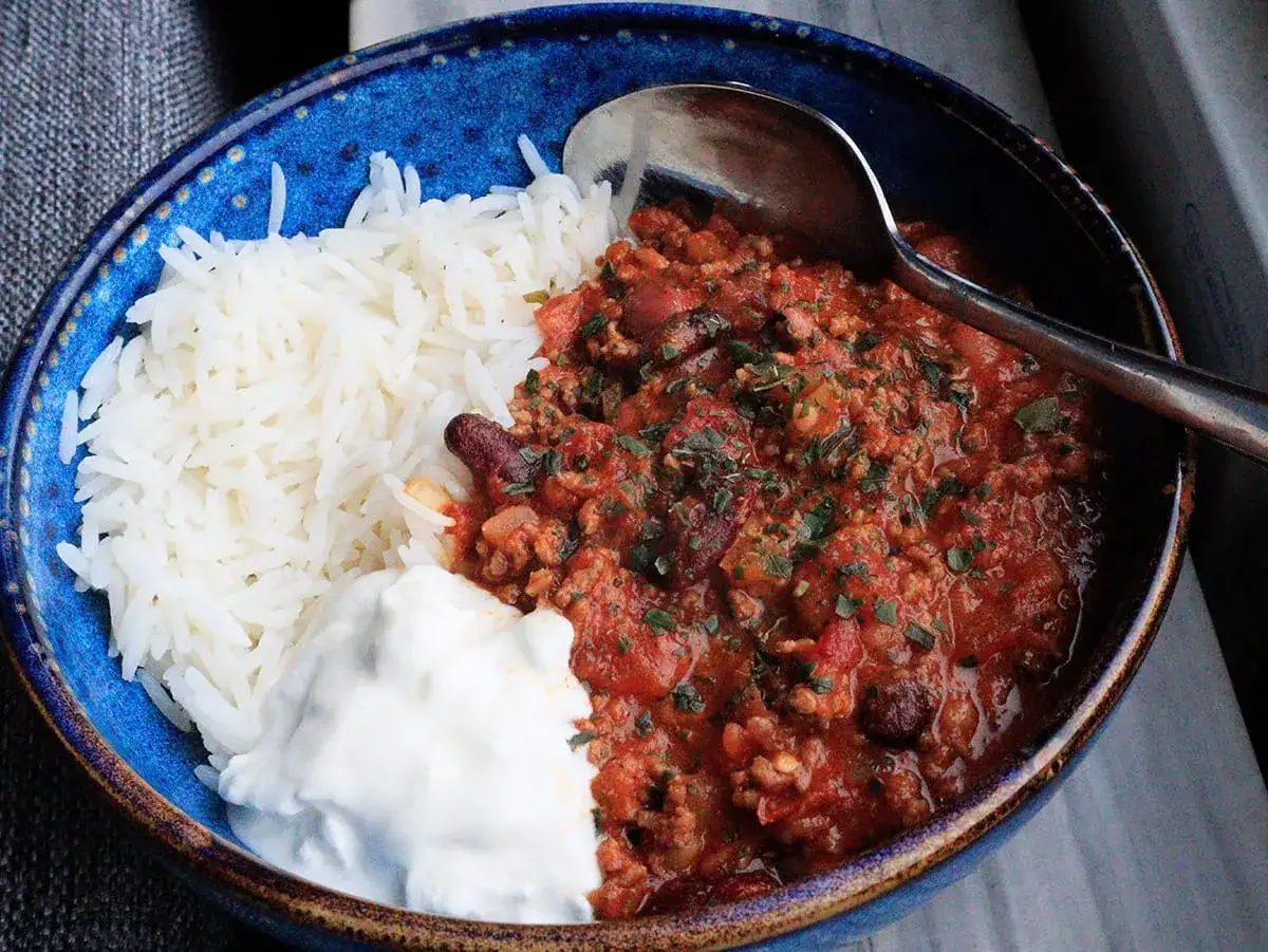 En blå skål med ris, en klick gräddfil och en generös portion chili con carne, redo att avnjutas.