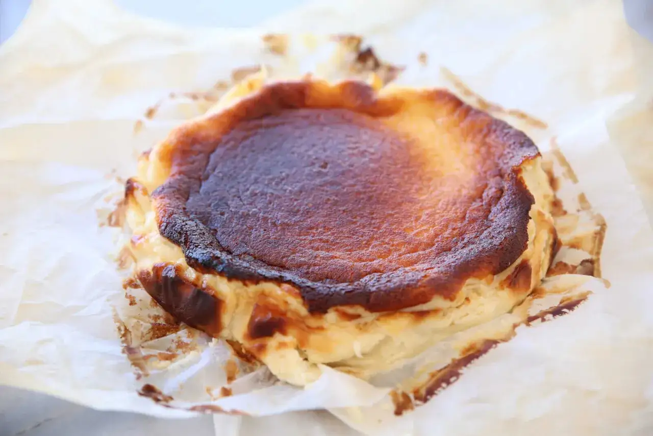 En perfekt karamelliserad baskisk cheesecake, med en mjuk och krämig insida, vilar på bakplåtspapper.