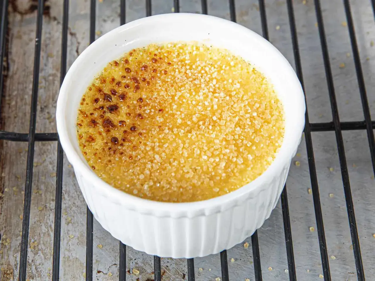 En vit skål med en perfekt karamelliserad creme brulee, med knäckig yta och gyllene socker.