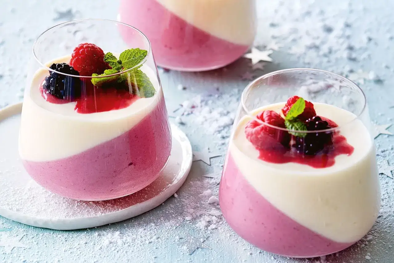 Två glas med vit chokladmousse och bär. En härlig dessert som passar perfekt till fest.