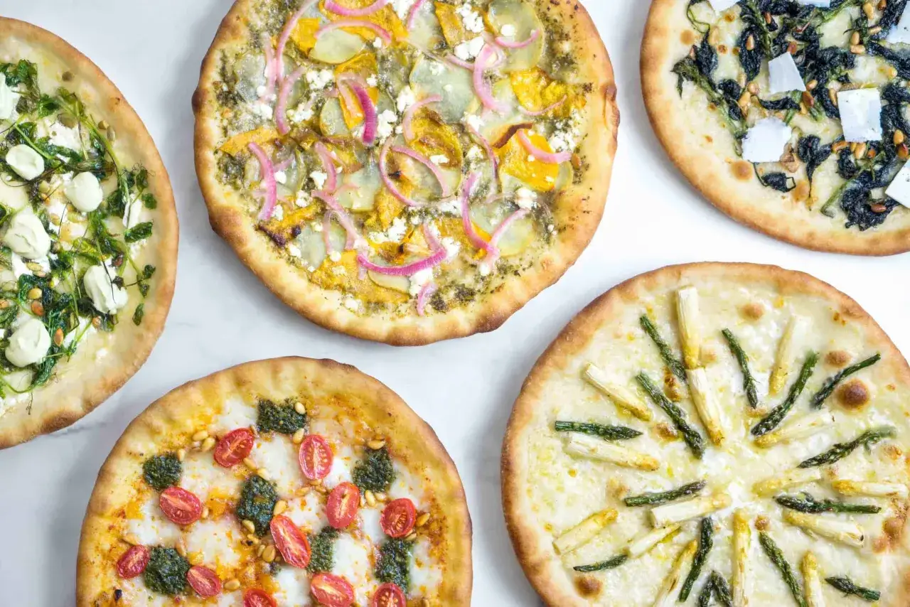 Fem olika pizzor med varierande egen pizza topping: sparris, tomater med pesto, spenat och ost, samt en med potatis och rödlök.