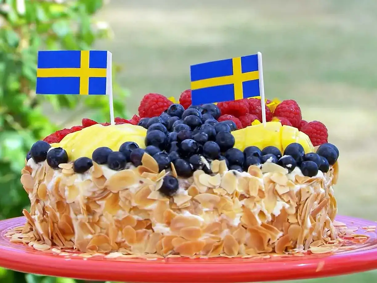 En vacker tårta med frukt och bär, dekorerad med svenska flaggor. Perfekt för en svensk högtid!