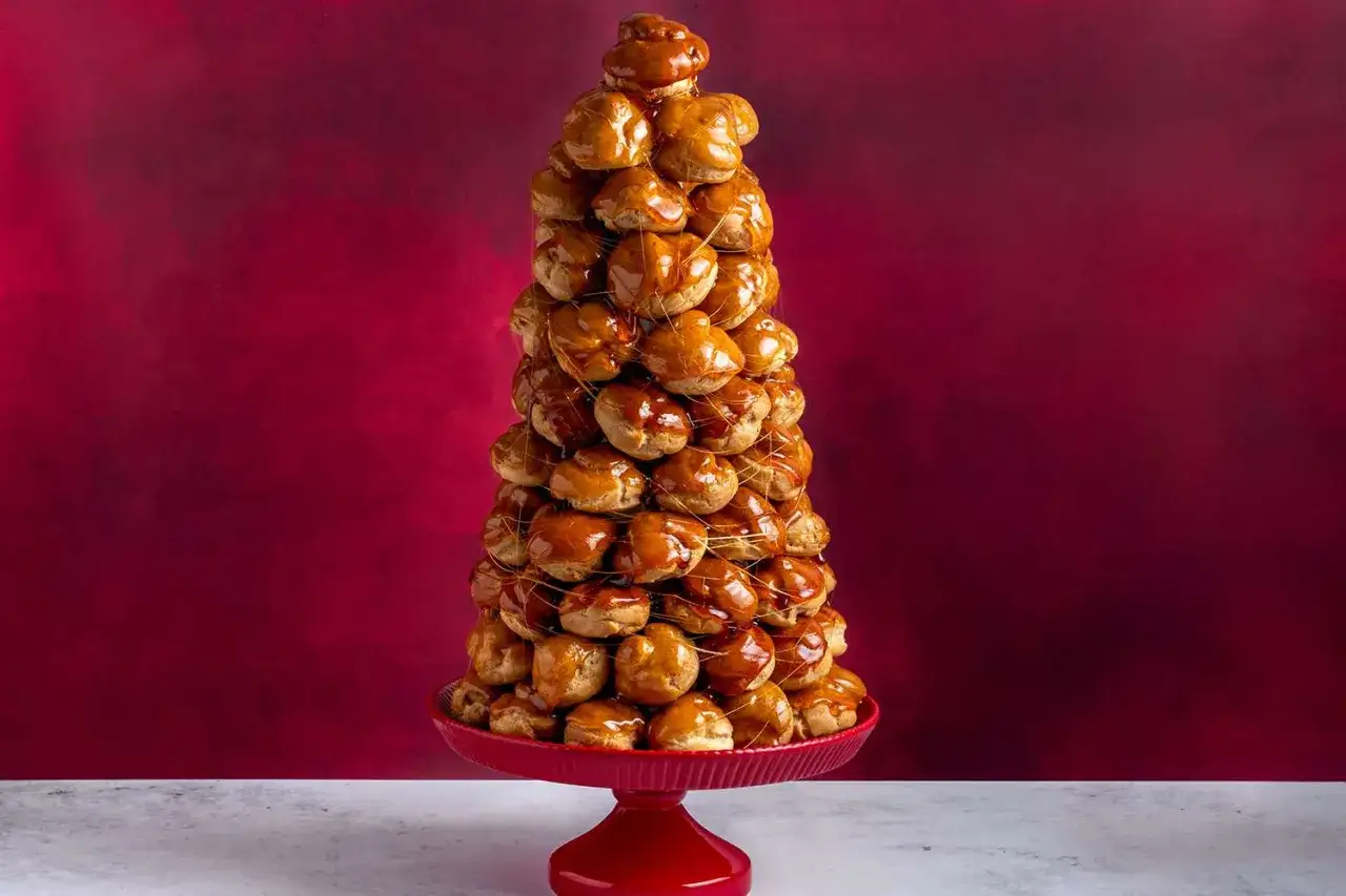 Ett imponerande torn av petit choux, glaserade med karamell, på ett rött fat mot en vinröd bakgrund.