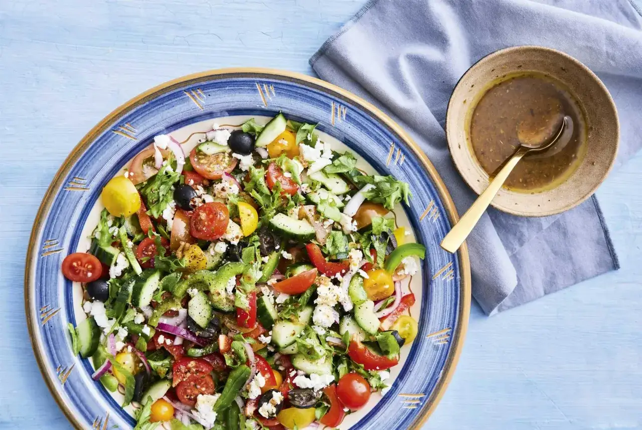 En härlig grekisk sallad med tomater, gurka, oliver, paprika och fetaost, serverad i en vacker blåmönstrad skål.