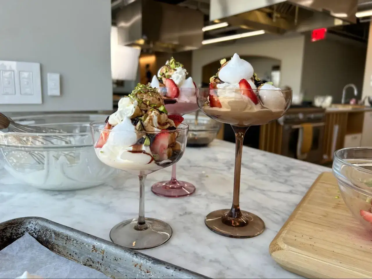 Tre eleganta glas med Eton Mess, fyllda med grädde, jordgubbar, maräng och pistagenötter.