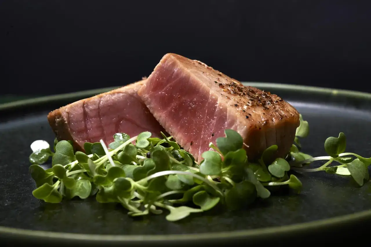 Två bitar perfekt stekt tonfisk med en rosa innertemp, kryddad med peppar, serveras på en bädd av gröna skott.