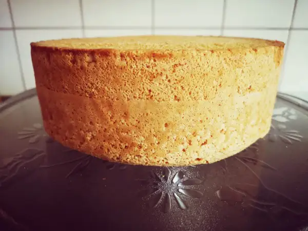 En gyllene anslag tårta med en porös textur står på ett mönstrat fat. Den är redo att dekoreras för ett speciellt tillfälle.