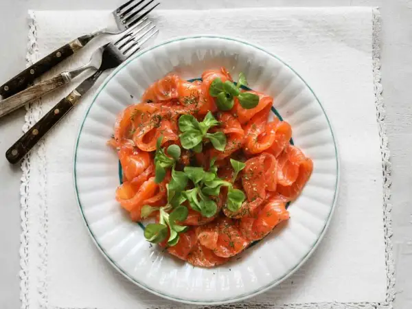 Vacker tallrik med gravad lax, garnerad med dill och gröna blad. Frågan är om man kan frysa gravad lax för att spara den till senare.