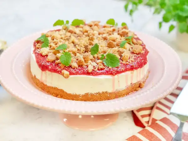 En krämig rabarber cheesecake med smulig topping och färska myntablad, serverad på ett rosa tårtfat.