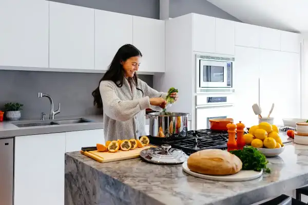 Kvinna lagar mat i ett modernt kök. Frukt, bröd och grönsaker ligger på bänken, bra spartips mat.